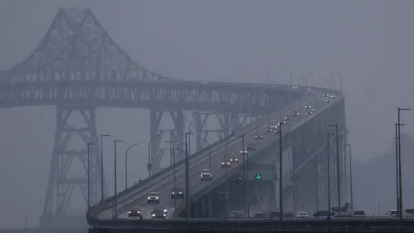 Cars drive over a bridge on a foggy day.