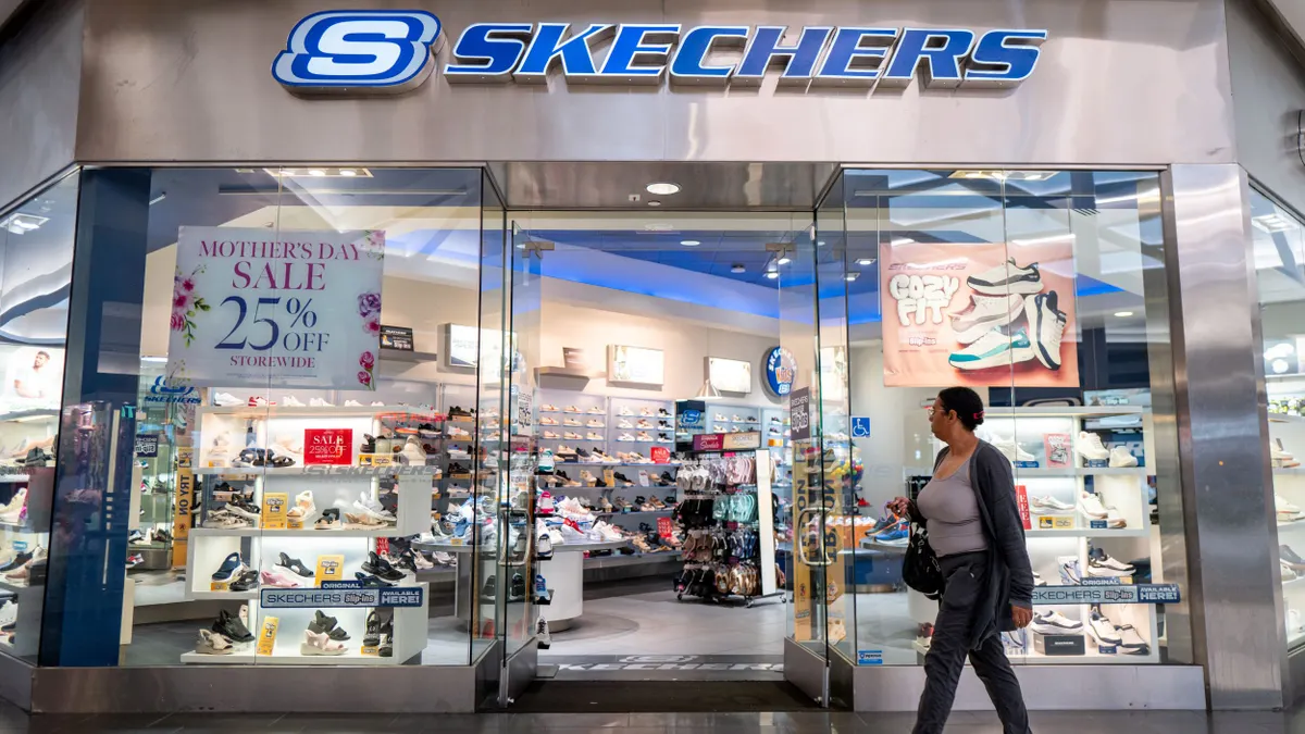 A person walks in front of a Skechers store in a mall.