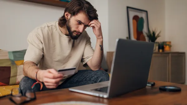 Worried man sitting on a couch looks at a laptop.