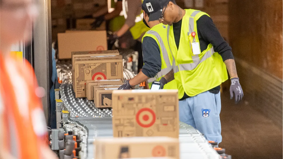 A worker in a yellow vest inspects a package with the Target logo as it makes its way down a conveyor belt.