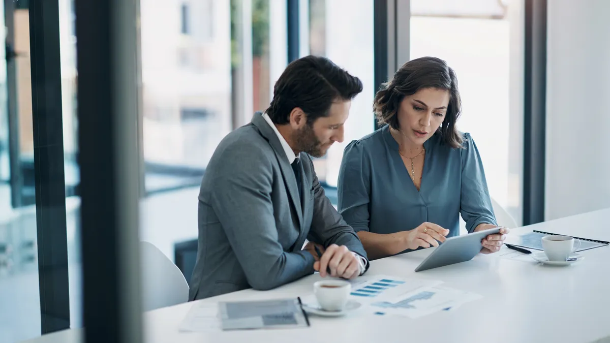 Business people sit at a table in an office planning budgets using a tablet and charts.