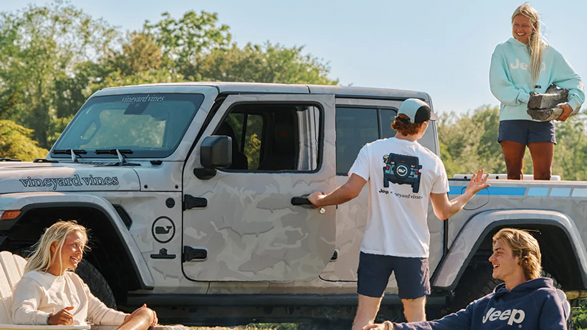 A group of people sitting around a bonfire wearing apparel items from Vineyard Vines and Jeep's capsule collection.