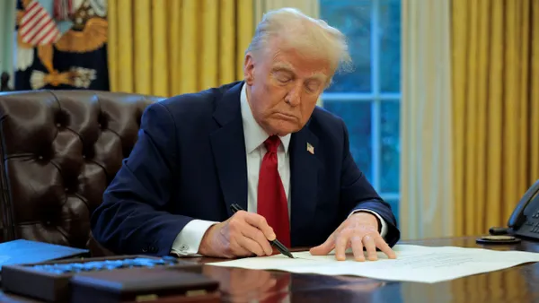 President Trump signs an executive order behind his desk in the oval office.