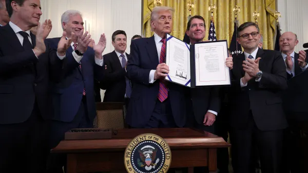 President Donald Trump signs Genius Act with congressional members around him in White House room.