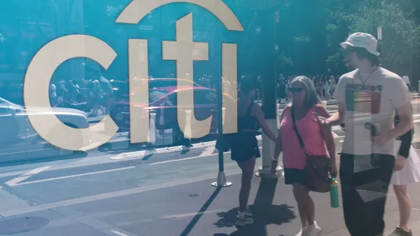 A glass window reflects an image of people and cards passing by on the street, with the "Citi" logo shown behind the window.