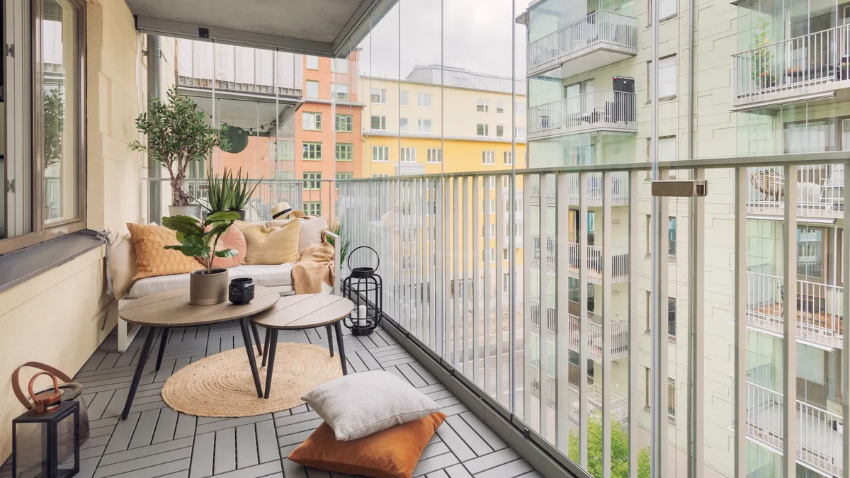 A large glass enclosed balcony with a small sofa, tables and various home decor.