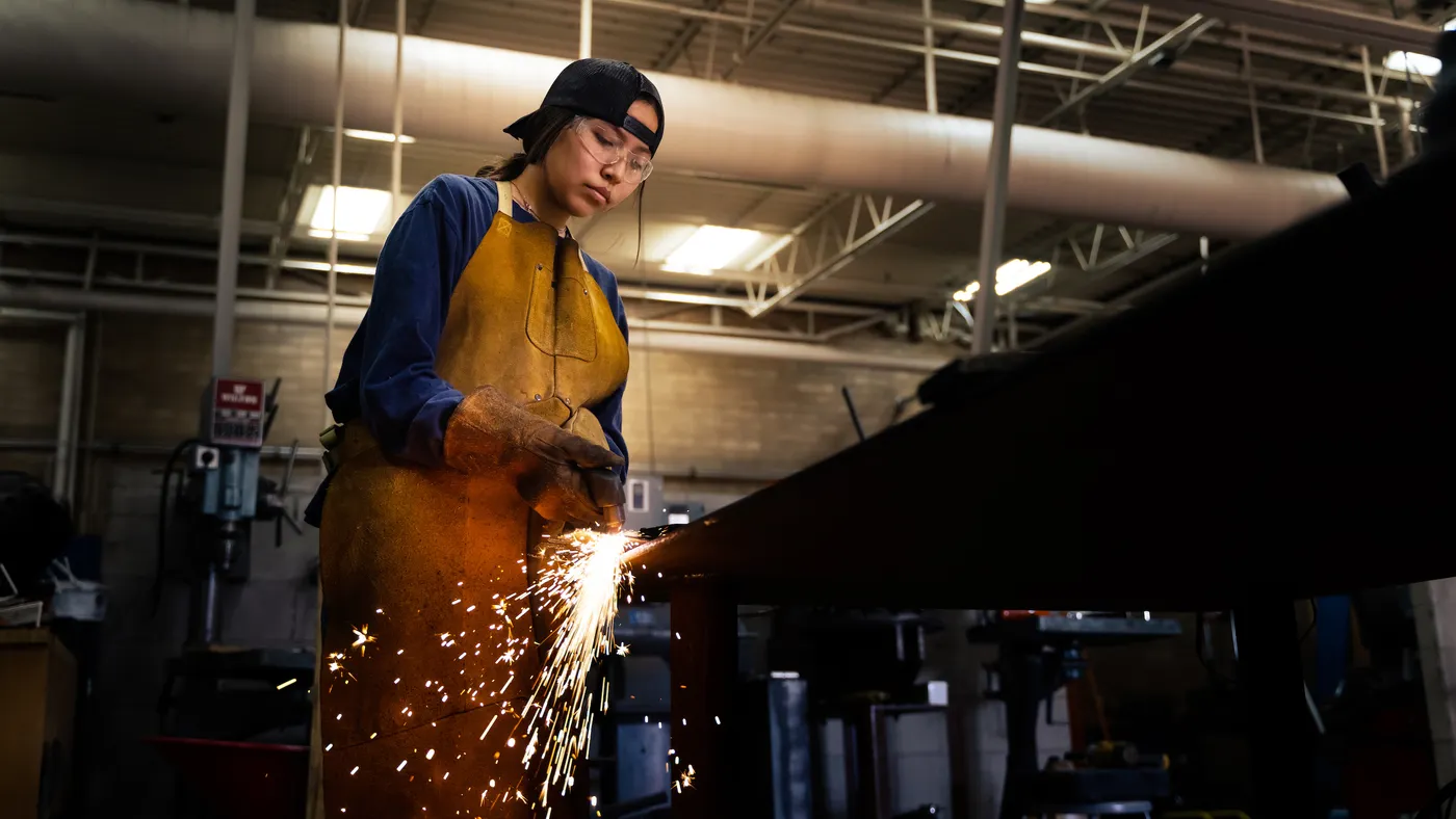 A person uses a torch cutter with a backwards hat in a manufacturing facility