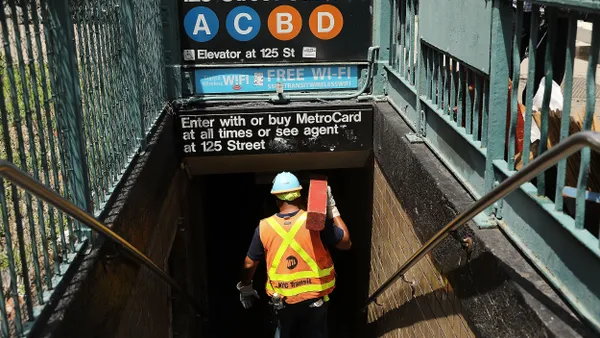 A man wearing a hardhat and safety vest climbs down the stairs to a subway station.