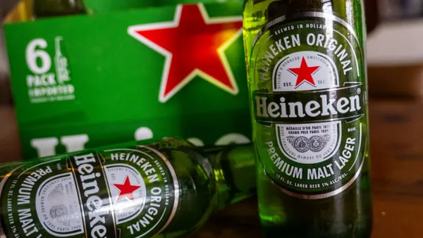 Two Heineken beer bottles are outside a six-pack carton.