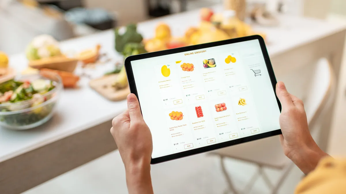 In a kitchen, close-up of hands holding a tablet with food on the screen.