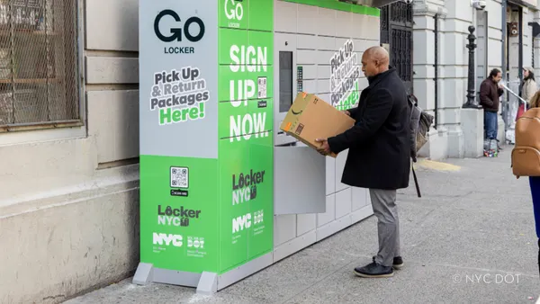 A person holds a package in front of a delivery locker location.