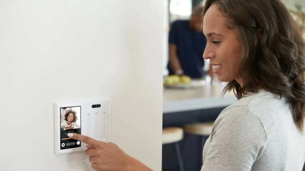 A person uses a wall-mounted smart home interface to answer a call in the kitchen.