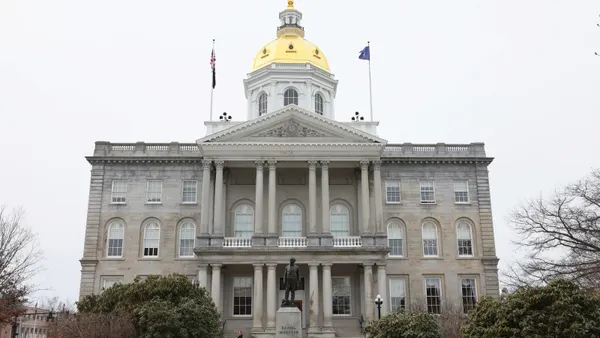 A statue sits on a pedestal in front of a columned government building with a gold dome