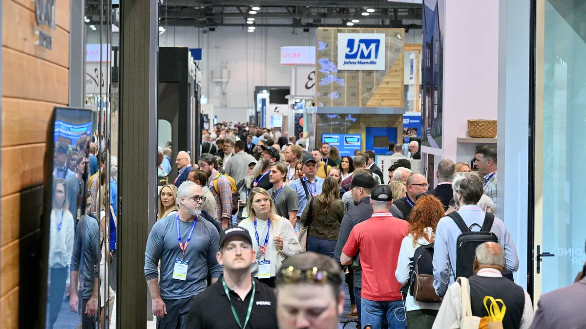 A crowd of people, many with lanyards, in a large room with banners hanging from the ceiling.