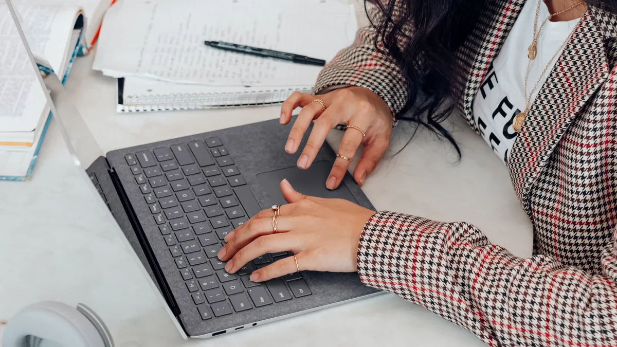 A feminine-presenting person types on a laptop