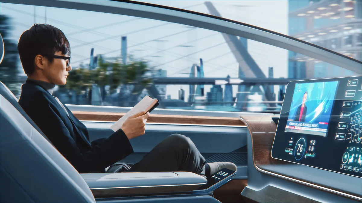 A stylish Japanese businessman in glasses reading a notebook and watching news on augmented reality screen while sitting in an autonomous self-driving zero-emissions car.