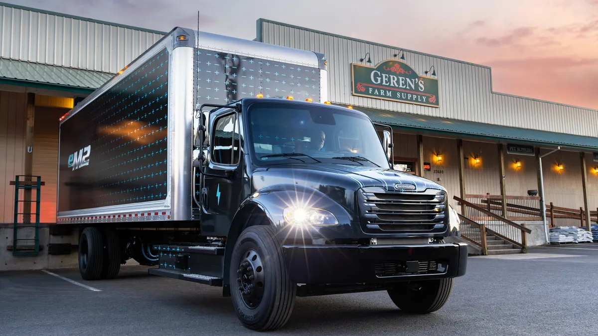 A driver sits in a Freightliner eM2 battery-electric medium duty truck in the parking lot of Gerens Farm Supply.