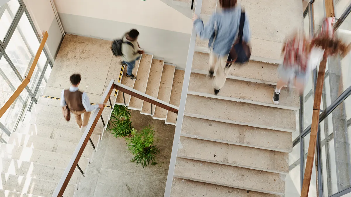 Several students walk up and down a staircase in a school hallway.