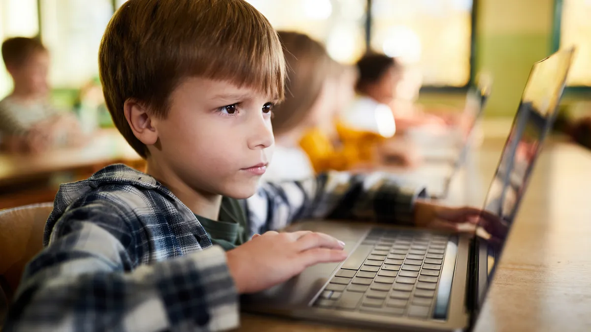 A student is stting at a desk looking at an opening laptop screen.