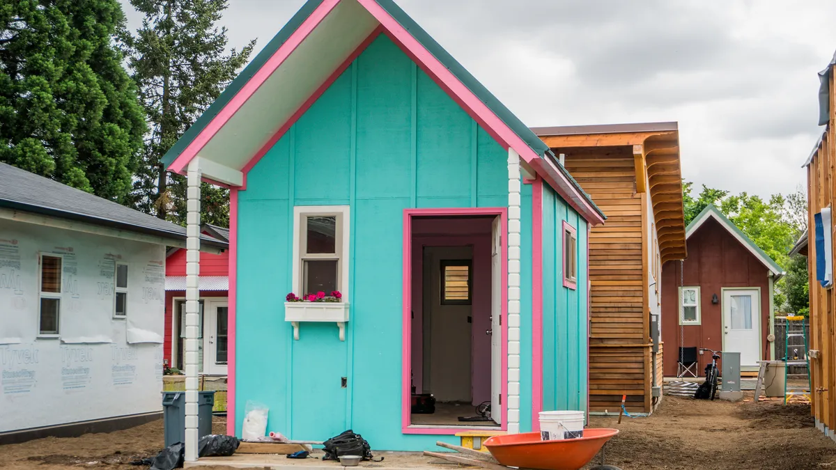 A colorful, peaked-roof tiny house with other tiny houses around it, designed to help transition homeless individuals into housing in Eugene, Oregon