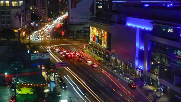 Cars at night with streaks of headlights and tail lights on a wide street with building on each side.