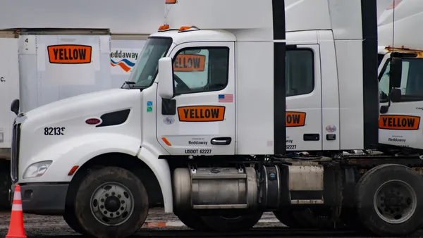 Empty Yellow Corp. tractors in a lot with an orange cone in the foreground.