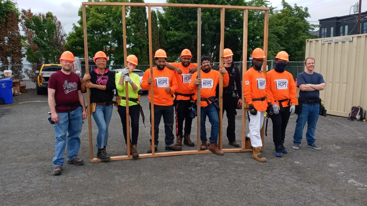 Several construction workers hold up a recently built wall structure.