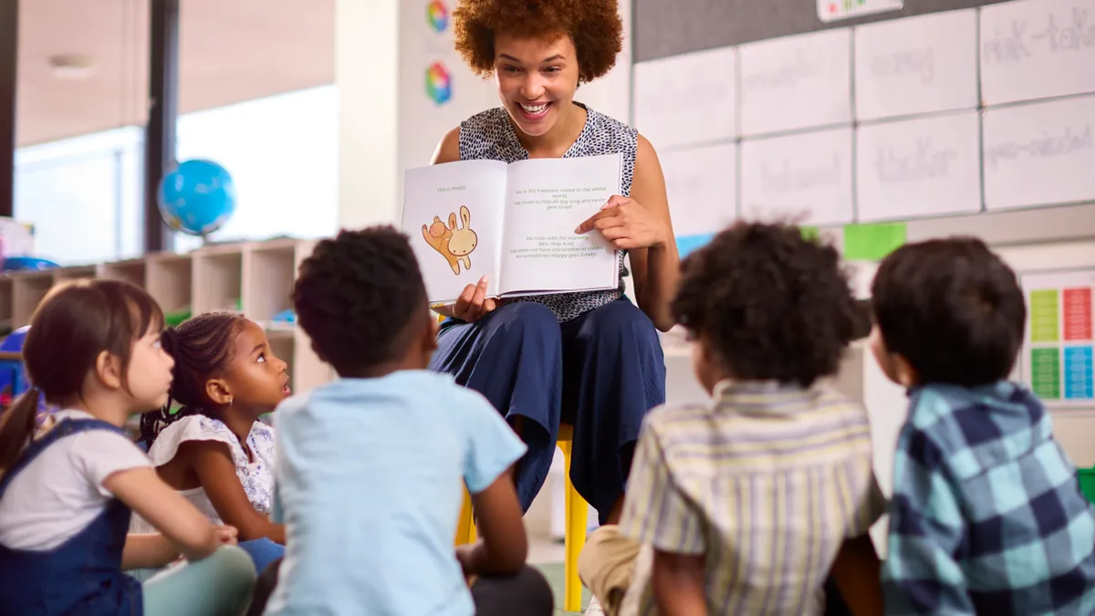 A teacher reads a picture book to a group of young students in a classroom setting.