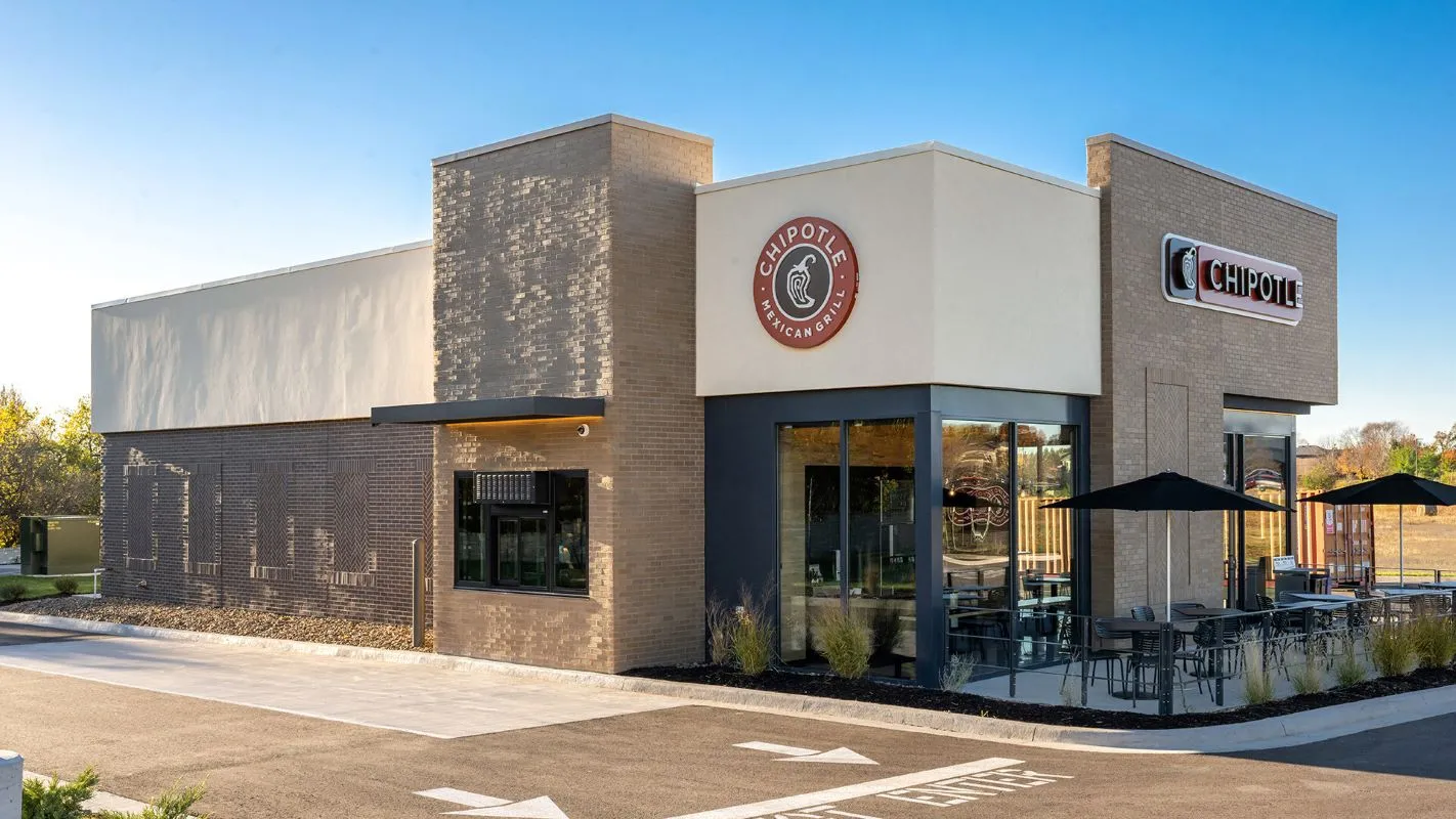 An image of a cream and beige building with a drive-thru lane. The building has a logo that says &quot;Chipotle.&quot;