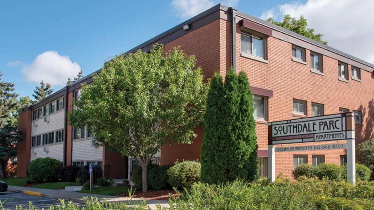 Three-story brown brick apartments surrounded by grass and trees