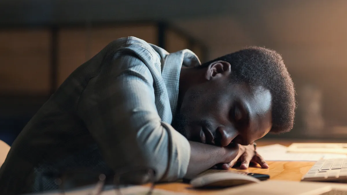 Black person, sleeping and burnout from working at night by office desk suffering stress or overworked.