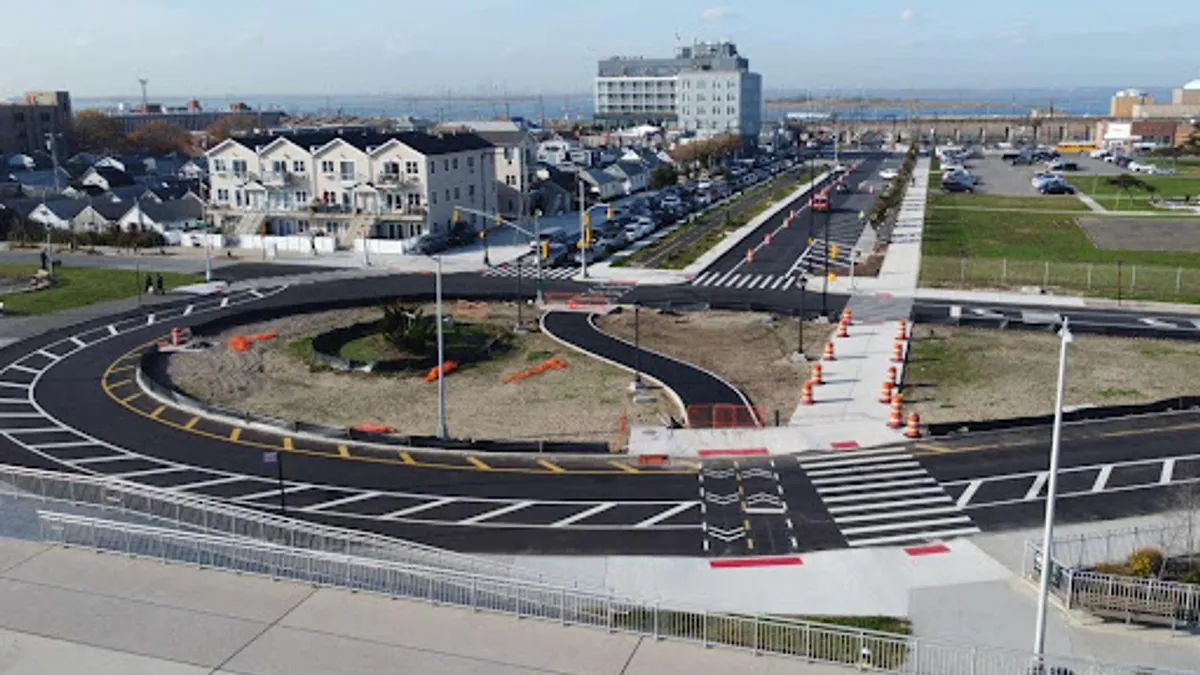 A curving road in front of duplexes, a tower in the background, and some green space to the side and in the background. The pavement is new, with fresh markings.