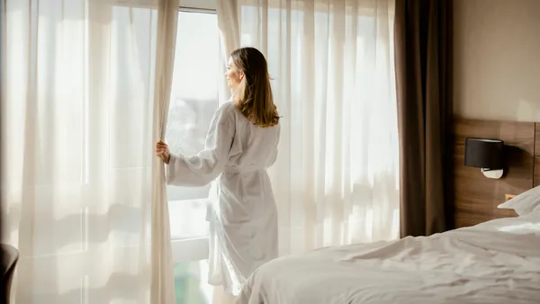 A woman looks out of a hotel room window.