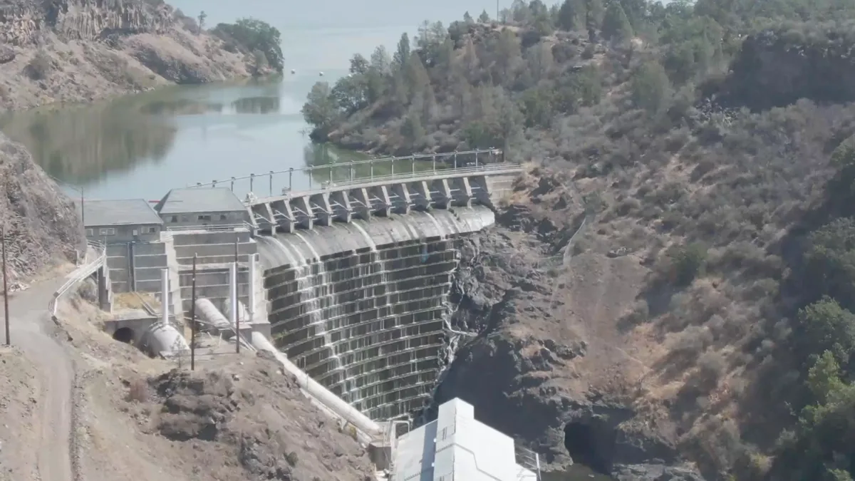 Aerial view of a towering dam, with river in foreground and background.