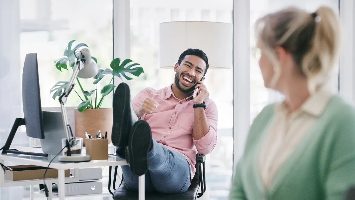 A person in the foreground looks back at another talking on a phone call with feet up.