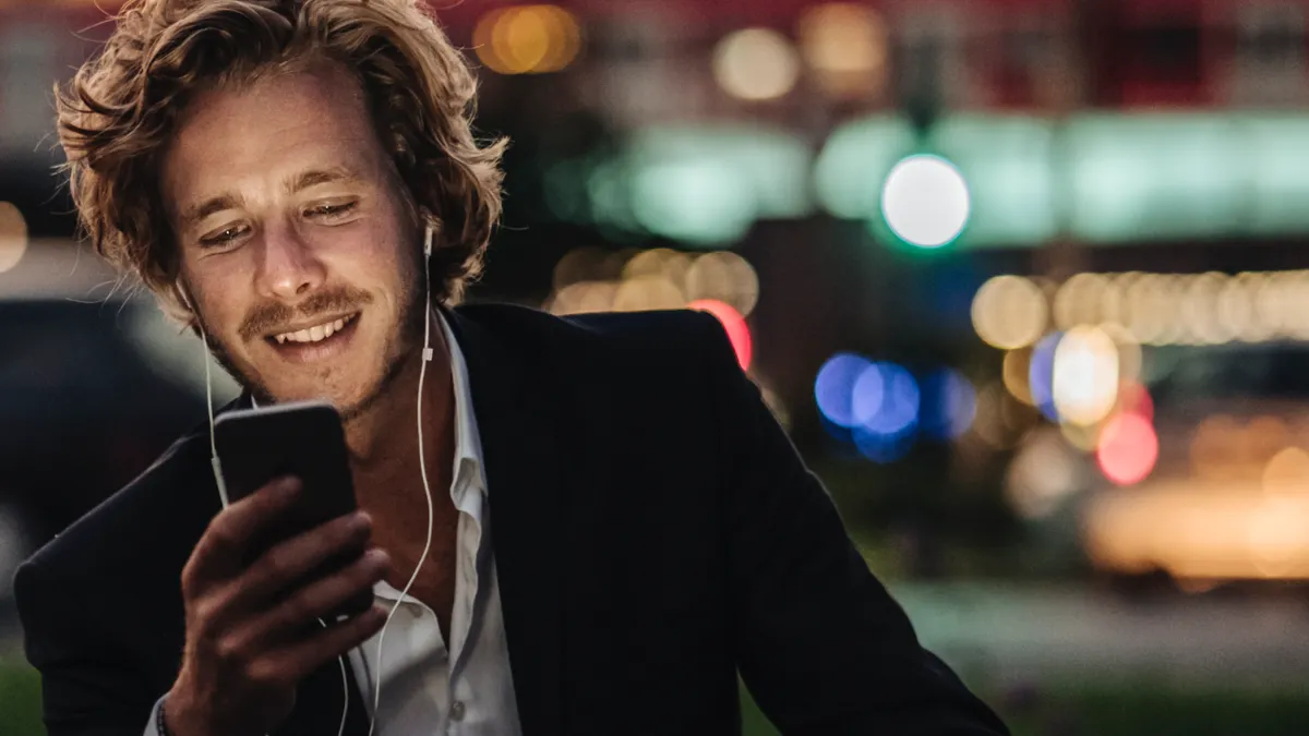 A man in a suit smiles while looking at his smartphone at night.