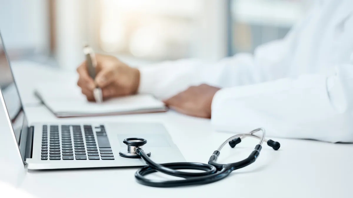 Laptop, stethoscope and doctor writing in notebook for research planning or medical tech innovation in hospital office.