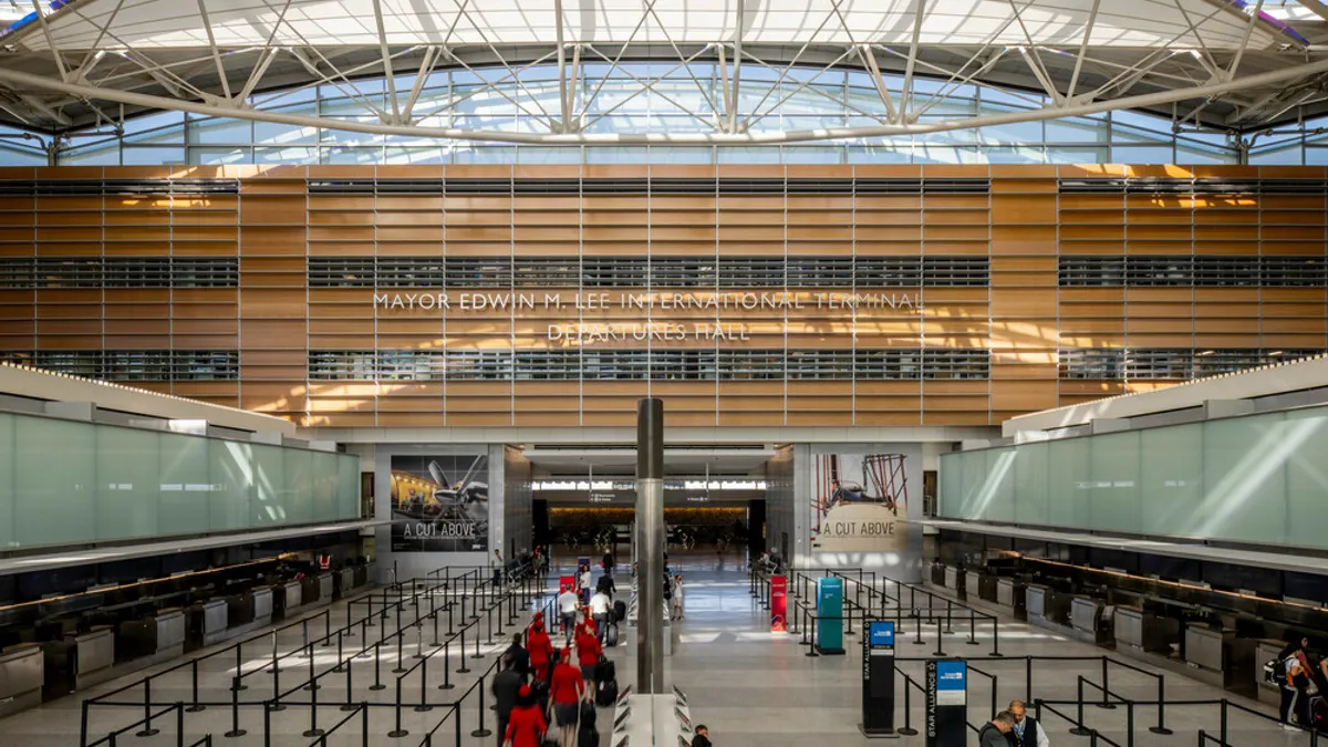 People filter through a mostly empty hall with a white, linoleum-esque floor and open ceiling via windows.