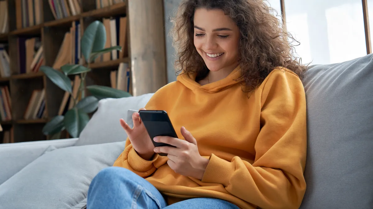 Happy millennial teen girl checking social media holding smartphone at home.