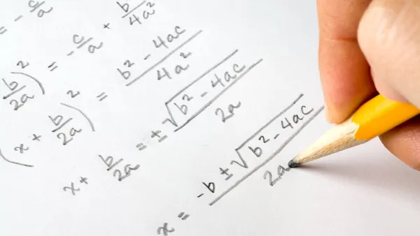 A hand holding a pencil is shown writing out algebra equations.