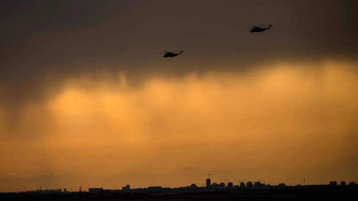 Helicopters fly through smoke-tinged air above a city.