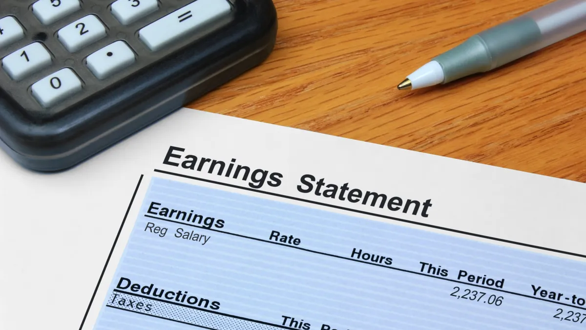 Paper personal earnings statement lays on desk next to pen and calculator.