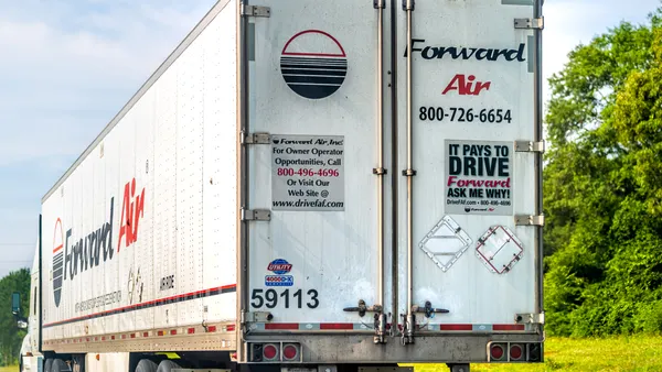 A Forward Air refrigerated trailer on the road with trees and shrubs in the background.