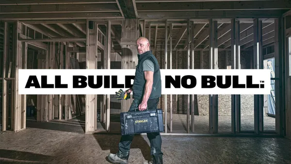A man midstride holds a toolbox in a construction site.