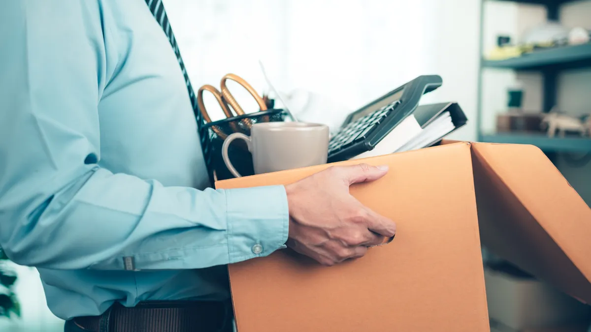 Person holds cardboard box containing office supplies.