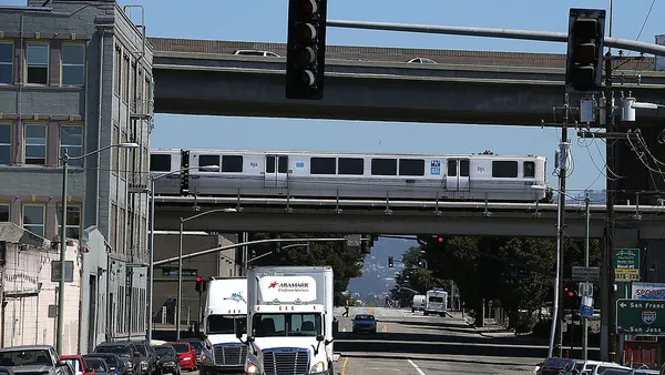 A silver bart train runs over a street.
