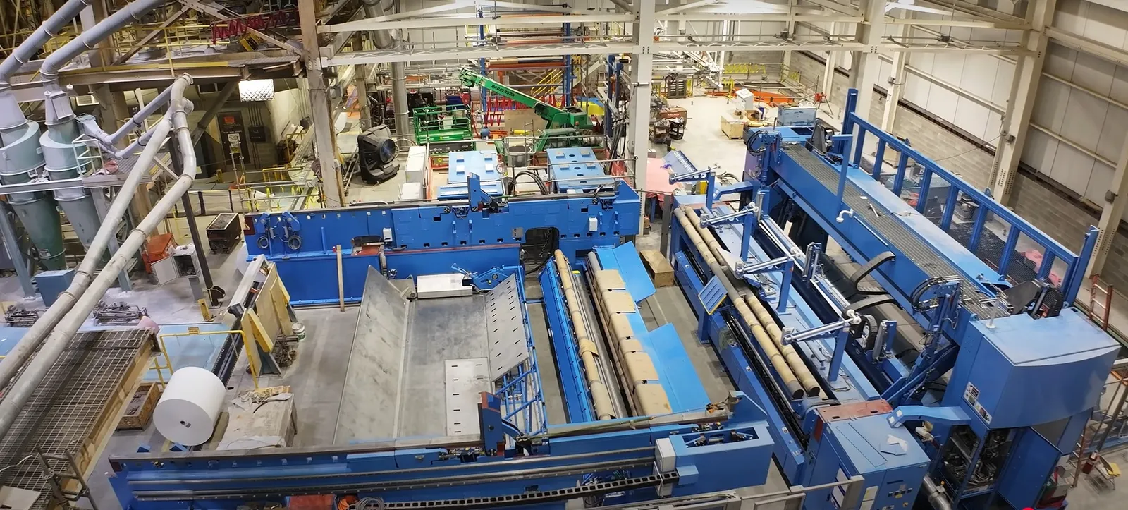 A large roll of white paper is next to industrial equipment in a manufacturing facility.