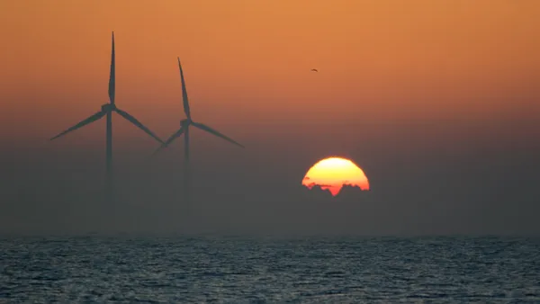 Two offshore wind turbines on the sea with a sunrise on the horizon.