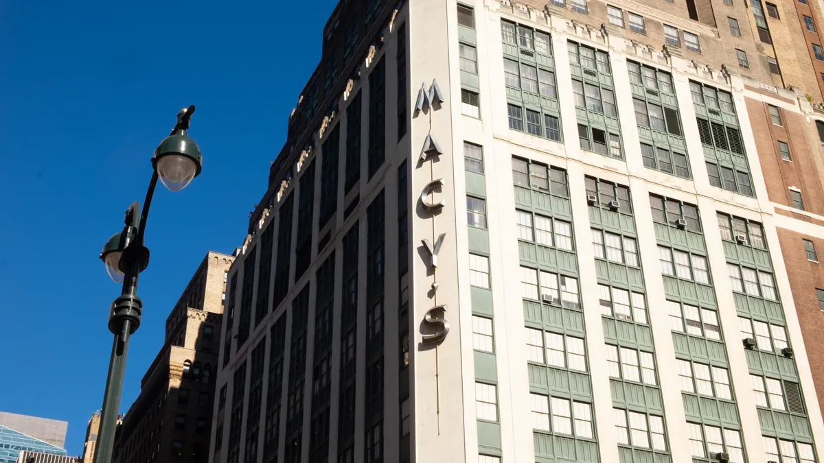 Against a blue sky, a street lamp to the side of a large department store building.