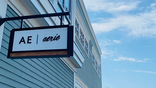 A sign posted on a blue-painted clapboard building says "AE" and "Aerie" as clouds drift in a blue sky.